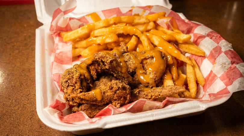 Golden fried chicken and french fries with cheese sauce in a red checkered takeout container.